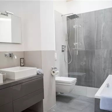 Ein modernes Badezimmer mit zwei Waschbecken, einer großen Dusche und einer Badewanne. Die Wände sind in neutralen Grautönen gehalten, was einen eleganten Look schafft.