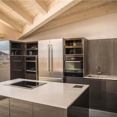 Moderne Küche mit einer großen Kochinsel und Edelstahlgeräten. Es gibt viel natürliches Licht durch die Fenster.