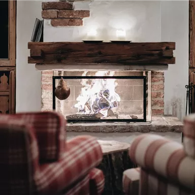 Ein gemütlicher Kamin mit flammendem Feuer in einem rustikalen Raum. Die bequemen Sessel schaffen eine einladende Atmosphäre.