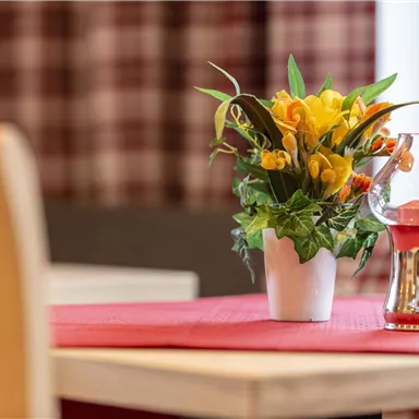 Ein schön dekorierter Tisch mit einem Blumentopf und einer Glasvase. Im Hintergrund sind karierte Vorhänge sichtbar.