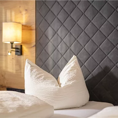 Ein gemütliches Schlafzimmer mit einem gepolsterten Kopfteil und hellen Kissen. Neben dem Bett befindet sich eine Wandlampe.