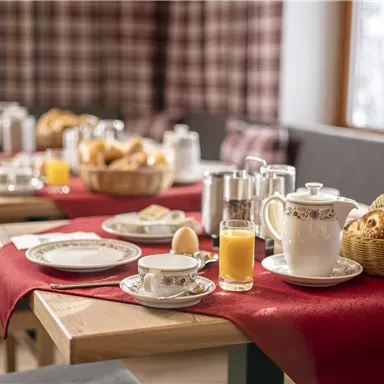 Ein gemütlicher Frühstückstisch mit Gebäck, einem Ei und Getränken. Das Ambiente ist warm und einladend.