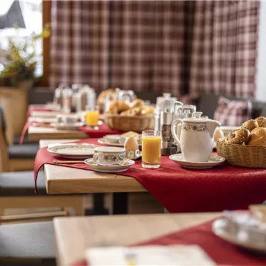 Ein schön dekorierter Frühstückstisch mit Brötchen, Käse und einem Krug Saft. Die Umgebung ist warm und einladend, ideal für einen gemütlichen Start in den Tag.