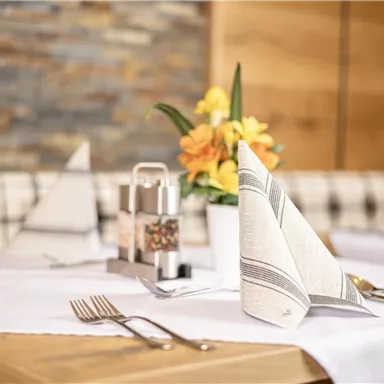 Ein stilvoll gedeckter Tisch mit feinen Servietten und Besteck. Eine blühende Pflanze in einer Vase ergänzt die elegante Tischdekoration.