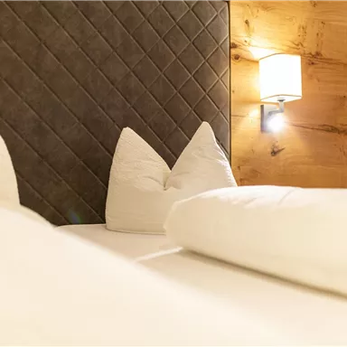 Ein gemütliches Schlafzimmer mit einem hellen Bett und dekorativen Kissen. Die Wände sind warm und ein Lichtschein sorgt für eine einladende Atmosphäre.