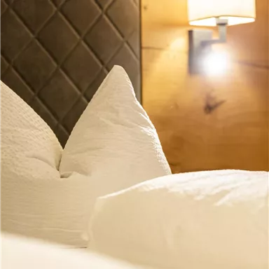 Ein gemütliches Schlafzimmer mit weißen Kissen und einer sanften Wandbeleuchtung. Die Holzverkleidung sorgt für eine warme Atmosphäre.