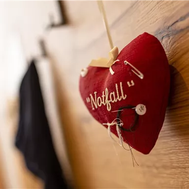 Ein rotes Herz hängt an der Wand und trägt das Wort "Notfall". Es ist mit einer Sicherheitsnadel und einem Faden dekoriert.