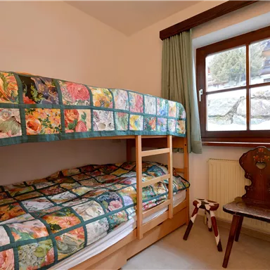 Ein gemütliches Schlafzimmer mit einem Etagenbett und bunten Bettwaren. Neben dem Bett steht ein Stuhl und ein Fenster bietet einen Blick nach draußen.