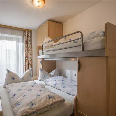 A cozy room with a bunk bed and two single beds. Large windows let in plenty of light, and the flower curtains give the room an inviting atmosphere.