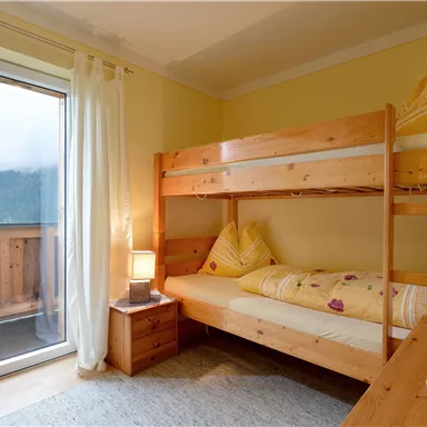 Ein gemütliches Schlafzimmer mit einem Etagenbett und einem großen Fenster. Die Wände sind in einem sanften Gelbton gestrichen und der Raum wirkt hell und einladend.