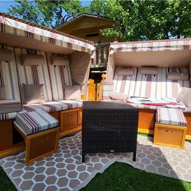 Zwei gemütliche Liegen mit gestreiften Kissen stehen im Garten. Ein kleiner Tisch aus Rattan ergänzt die entspannte Atmosphäre.