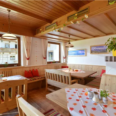 Ein gemütliches Restaurant mit Holzmöbeln und warmem Licht. Die Fenster bieten einen Blick auf die Umgebung, während Tischdecken mit Blumenmotiven dekoriert sind.