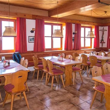 A cozy restaurant with wooden chairs and tables. The large windows let in plenty of daylight and the red curtains create a warm atmosphere.