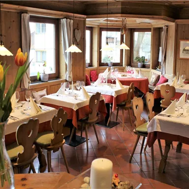 Ein gemütliches Restaurant mit Holzwänden und eleganten Tischen. Blumen schmücken die Tische und das Licht sorgt für eine einladende Atmosphäre.