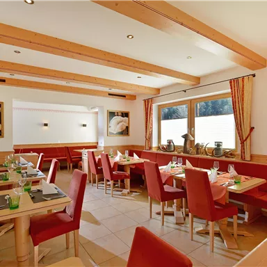 A cozy restaurant with a wooden ceiling, red benches, and an inviting atmosphere. The tables are neatly set and decorated.