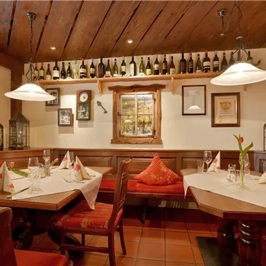 A cozy restaurant with wooden decor and elegant tables. Wine bottles and decorative elements are on the walls.