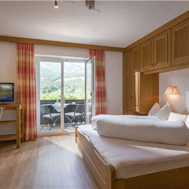 A comfortable hotel room with a large bed and a television. The room has a balcony overlooking nature.
