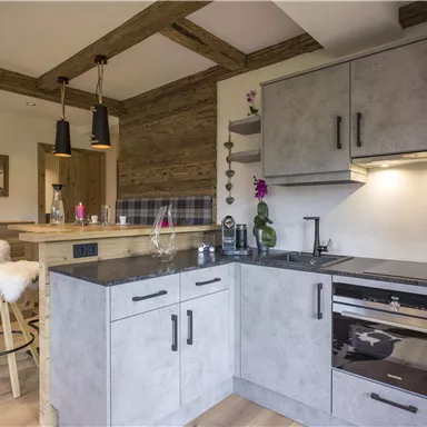 A modern kitchen with gray furniture and an elegant countertop. The space has a cozy atmosphere with wooden beams and a bar area.