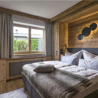 A cozy bedroom with wooden decor and a large window. The rooms are bright and inviting, ideal for a relaxing stay.
