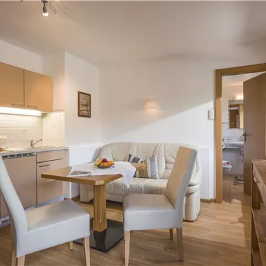 A cozy living room with a small kitchenette and a dining table. Bright furniture and a television create an inviting atmosphere.