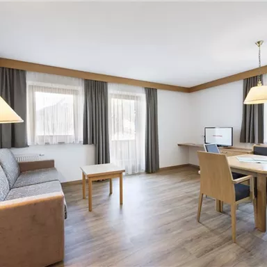 Ein modernes Wohnzimmer mit einer gemütlichen Sitzecke und einem Essbereich. Helle Fenster sorgen für eine freundliche Atmosphäre.