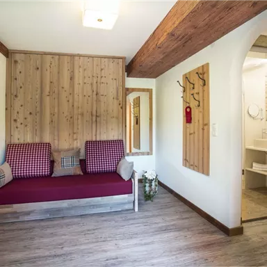 A cozy room with wood paneling and a red bench. On the right side, a bathroom is visible.