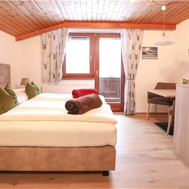 A bright, modernly furnished bedroom with two beds. The room has large windows and a cozy atmosphere.