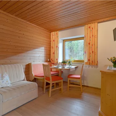 Ein gemütlicher Raum mit Holzwänden und einem Sofa. Es gibt einen Essbereich mit Holztisch und Stühlen sowie einen Fernseher an der Wand.