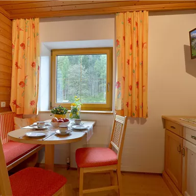 Ein gemütlicher Essbereich mit einem runden Tisch und roten Stühlen. Der Raum ist hell und hat ein Fenster mit Blick ins Grüne.