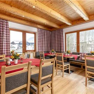 Ein gemütlicher Essraum mit Holzdecke und großen Fenstern. Die Tische sind dekoriert und bereit für Gäste.