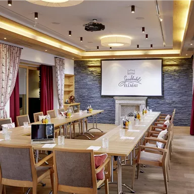 An elegant conference room with a long table and chairs. There is a screen on the wall for presentations.