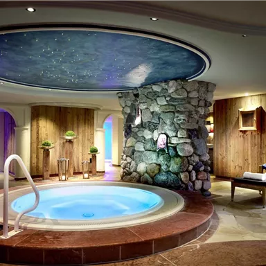 A relaxing spa with a circular hot tub and an artistically designed ceiling fresco. The natural stones and warm wood elements create a cozy atmosphere.