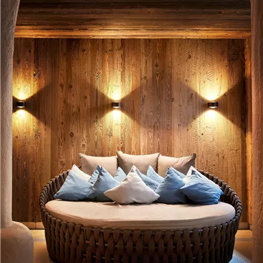 A cozy round seating area with many cushions. The walls are made of wood, and warm light creates a relaxed atmosphere.