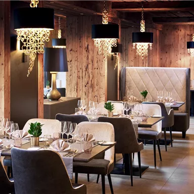 An elegant restaurant with wooden paneling and stylish lamps. The tables are thoughtfully set and create an inviting atmosphere.