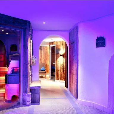 A modern wellness area with soft, purple lighting and stylish wooden details. The corridor leads to various treatment rooms and creates a relaxing atmosphere.