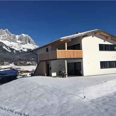 A modern house in a snowy landscape. In the background, impressive mountains can be seen.
