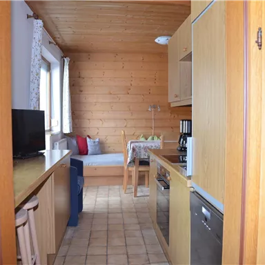 A cozy kitchen with wooden paneling and modern interior. On the left side, there is a television, and there is a seating area with a table and chairs.
