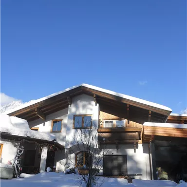 Ein schönes Haus im Schnee mit einem klaren blauen Himmel. Die Umgebung ist winterlich und friedlich.