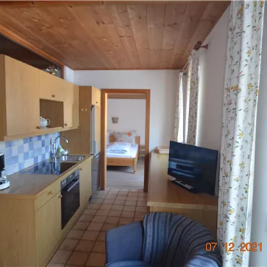 A cozy holiday apartment with a kitchenette and a living area. In the background, there is a bedroom with a double bed.