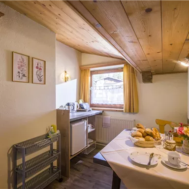 A cozy dining area with wooden ceilings and natural light. The table is set with breakfast pastries and flowers.
