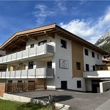 Ein modernes Gebäude mit Holz- und Steinarchitektur in den Bergen. Es hat Balkone und eine schöne Umgebung mit grünem Gras.