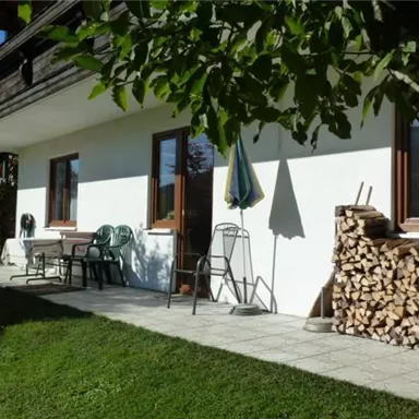 Eine gemütliche Terrasse mit Stühlen und einem Holzstapel. Der Garten ist grün und sonnig, ideal zum Entspannen.