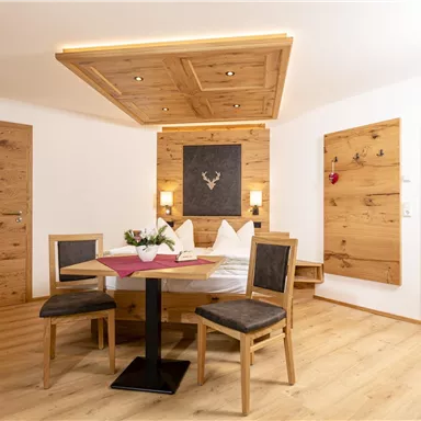 Ein gemütliches Zimmer mit Holzverkleidung und modernen Möbeln. Der Esstisch ist mit einer Blumenvase dekoriert und es gibt einen großen Spiegel an der Wand.