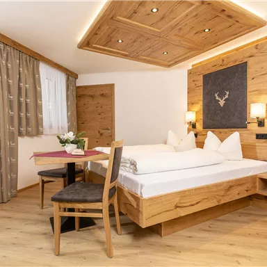 Ein gemütliches Zimmer mit Holzdekor und einem großen Fenster. Es enthält ein Doppelbett, einen Tisch und Stühle für eine einladende Atmosphäre.