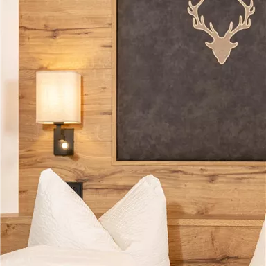 Ein gemütliches Schlafzimmer mit Holzdekor und einem stilvollen Hirschgeweih als Wandkunst. Auf dem Bett liegen große, weiße Kissen.