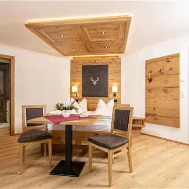 Ein gemütliches Zimmer mit Holzmöbeln und einem runden Tisch. Die warme Atmosphäre wird durch sanftes Licht und eine rustikale Dekoration betont.