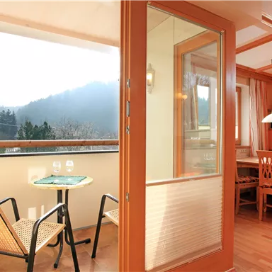 Eine helle Wohnung mit einem Balkon, von dem aus man die Berge sieht. Der Raum ist modern eingerichtet mit einem Tisch und Stühlen.