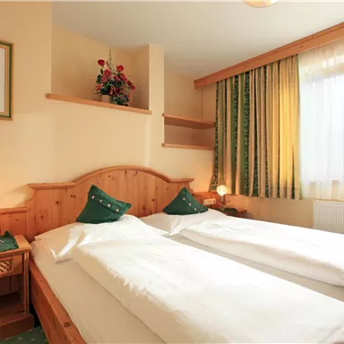 Ein gemütliches Zimmer mit zwei Einzelbetten und einer warmen Atmosphäre. Das Zimmer ist mit Pflanzen und weichen Vorhängen dekoriert.