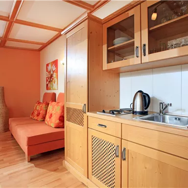 Eine gemütliche Küchenecke mit Holzmöbeln und einer kleinen Sitzecke. Die Wände sind in warmen Orange- und Brauntönen gehalten.