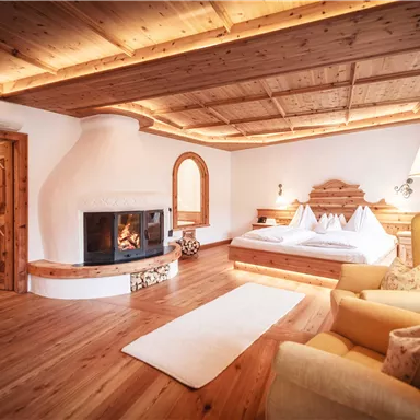 A cozy room with a large bed and a beautiful fireplace. Wood paneling and a soft carpet create a warm atmosphere.